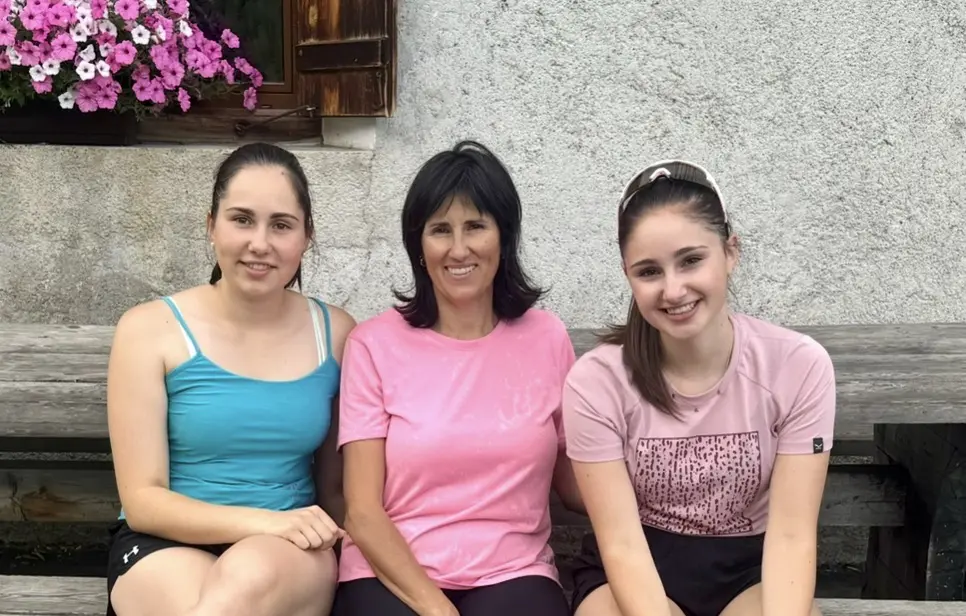 Martina, Lea und Sara Tondelli, die Gastgeberinnen der Montoni Chalets, sitzen lächelnd nebeneinander auf einer Bank.