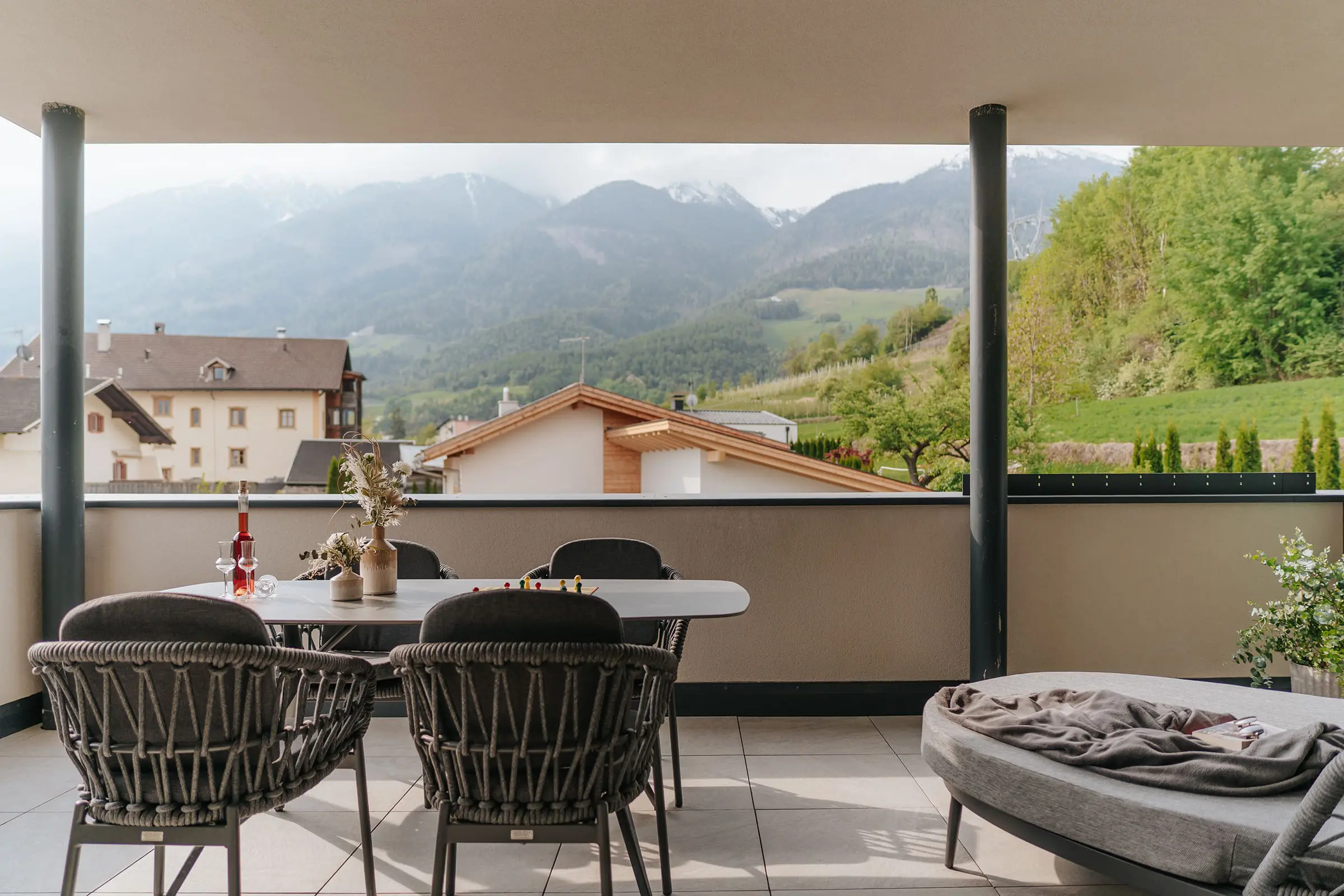 Grande terrazza con comodi mobili lounge e vista sui prati, sulle montagne e sul paese di Agumes, negli appartamenti Montoni Chalets a Prato allo Stelvio.