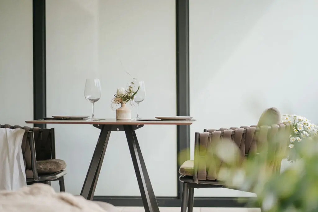 Gedeckter Tisch mit Blumenvase und zwei gepolsterten Stühlen auf der Terrasse einer Ferienwohnung der Montoni Chalets.