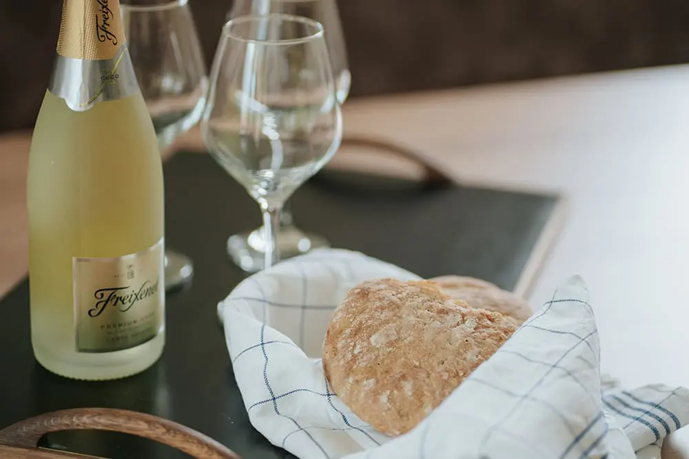 Fresh bread and a bottle of Prosecco on the table of a stylish Montoni Chalets holiday apartment in Vinschgau.