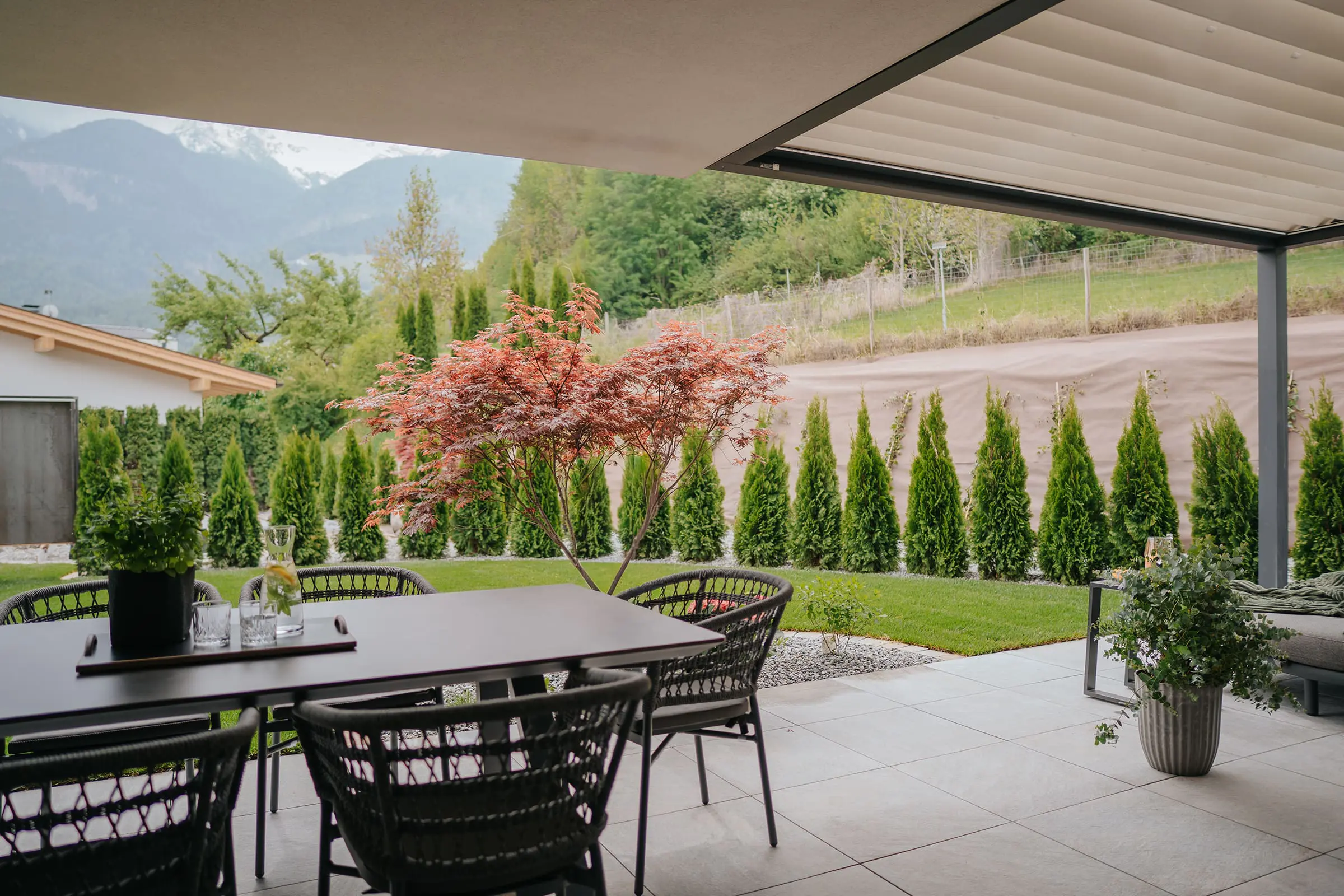 Große überdachte Terrasse vor einem Garten mit vielen Bäumen in einer Ferienwohnung der Montoni Chalets in Prad am Stilfserjoch.