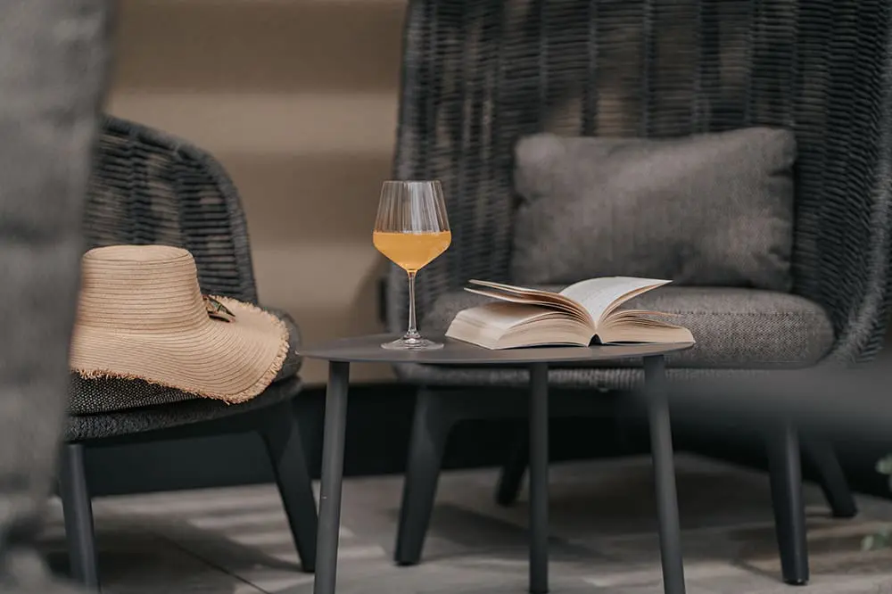 Cosy seating area with lounge chairs, an open book and a drink on the terrace of a Montoni Chalets holiday apartment in Prad am Stilfserjoch.