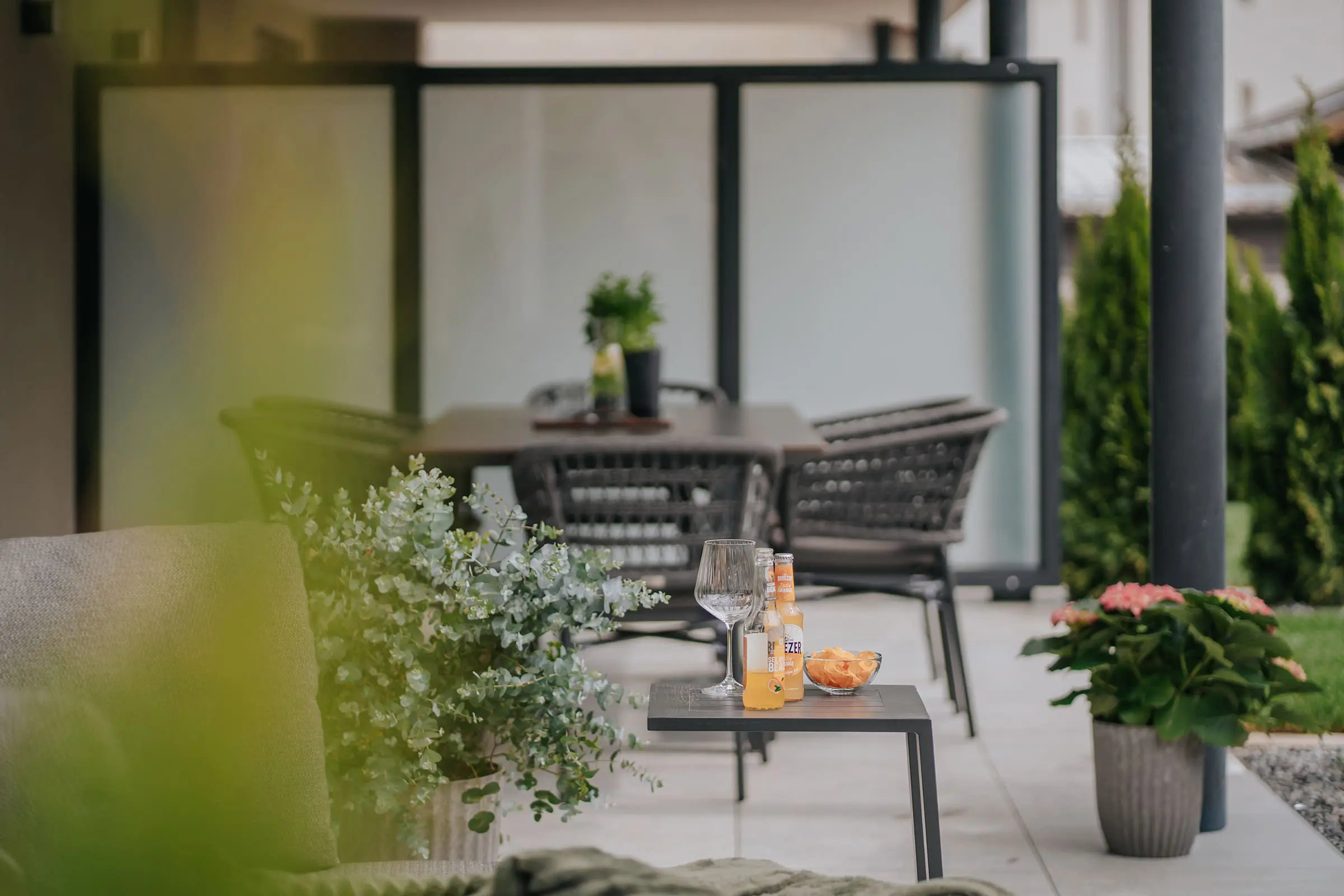 Grande terrazza con accogliente zona pranzo e lounge, diverse piante e vista sul giardino nell'Appartamento Solis nei Montoni Chalets.