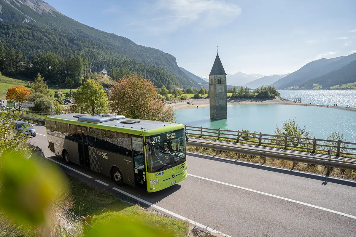 Öffentlicher Linienbus fährt am versunkenen Kirchturm im Reschensee im Vinschgau vorbei.